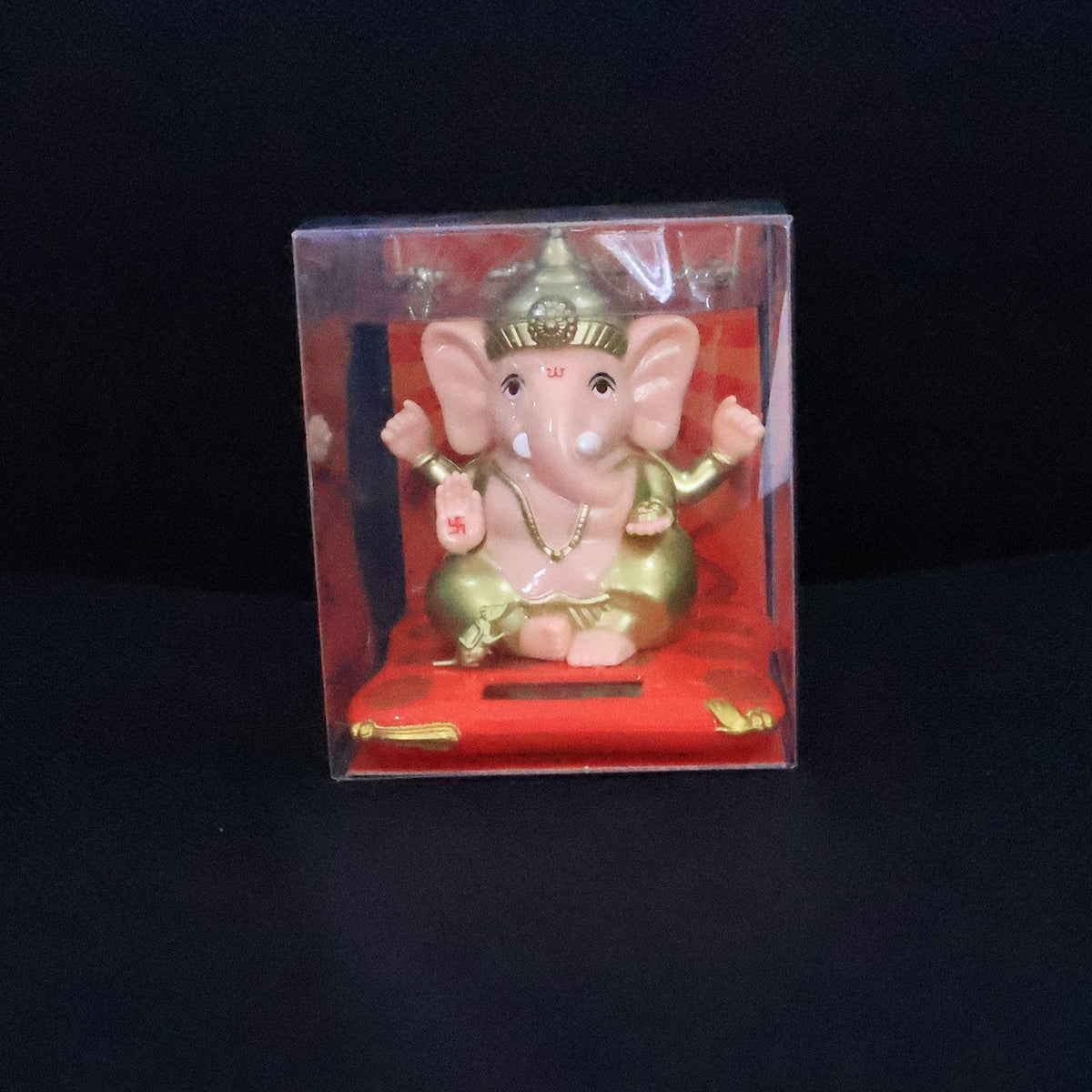 A Ganesha idol on a red base, packaged inside a clear plastic box against a dark background.