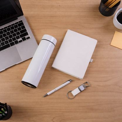 Overhead view of a white thermal bottle, notebook, pen, and keychain on a light wooden desk with laptop.
