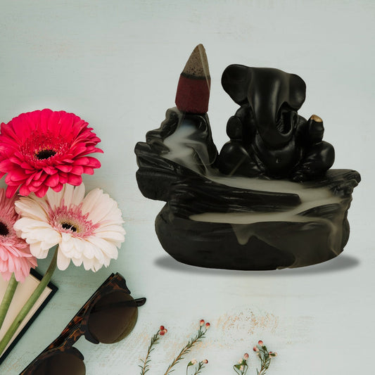 Black Ganesha smoke fountain with a lit incense cone and flowing smoke, surrounded by pink and white flowers, sunglasses,