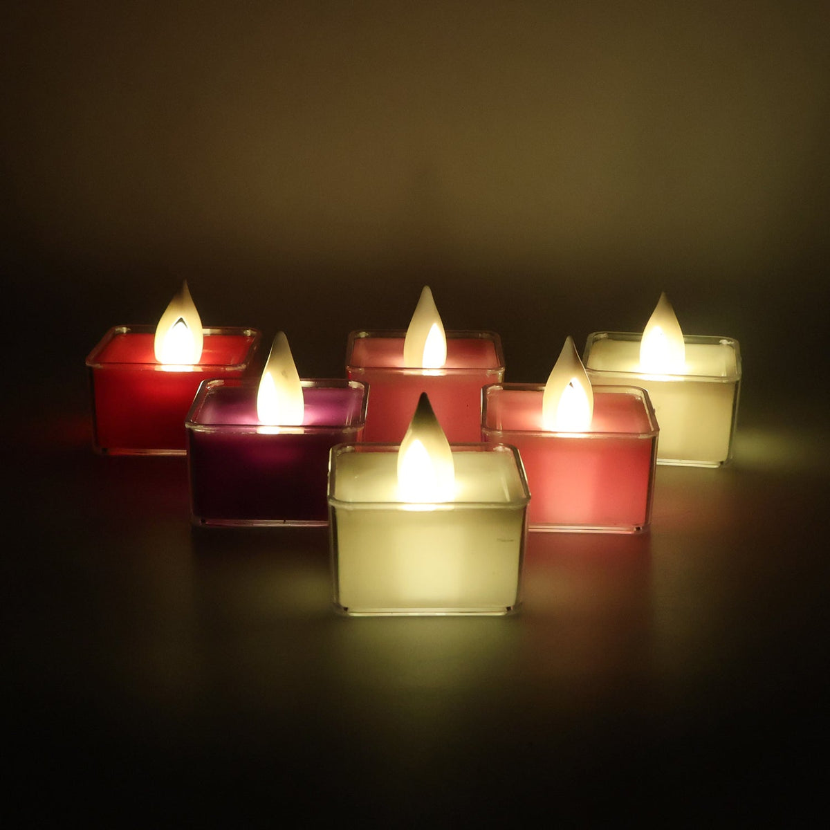 Six square LED flameless tealight candles glowing in various colors, arranged in a scattered pattern on a dark surface.