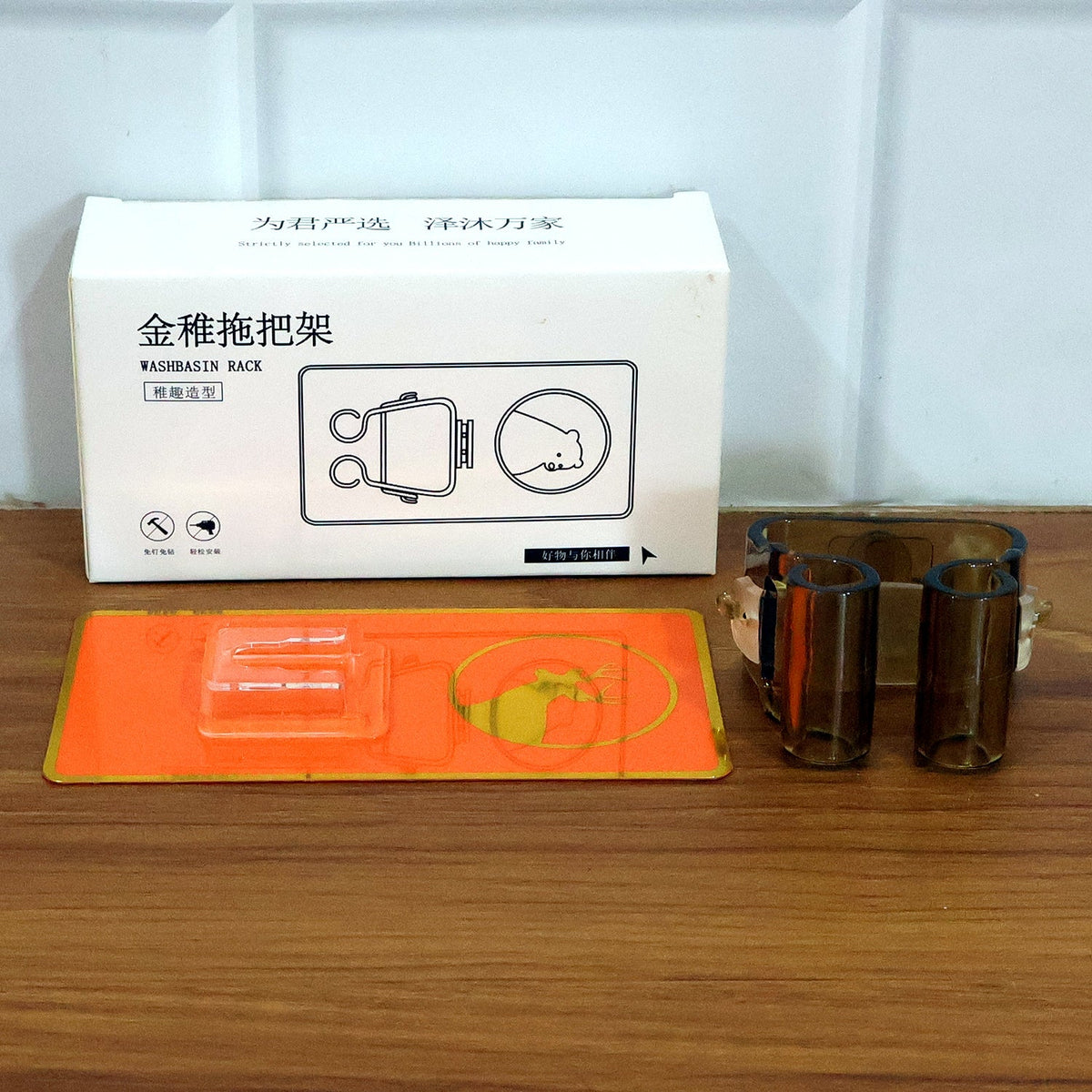 The orange deer-themed wall-mounted holder, its adhesive backing, and a white product box with instructions on a wooden