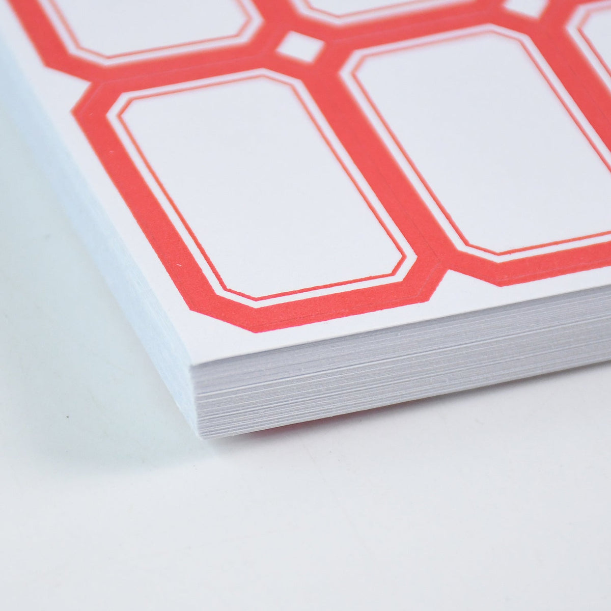 Close-up view of the corner of a stack of white labels with red borders.