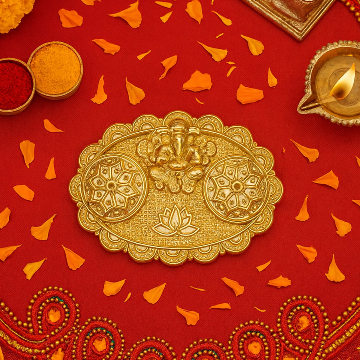 A gold-finished chopra with Ganesh and ornate containers on a red fabric, surrounded by scattered orange flower petals and a
