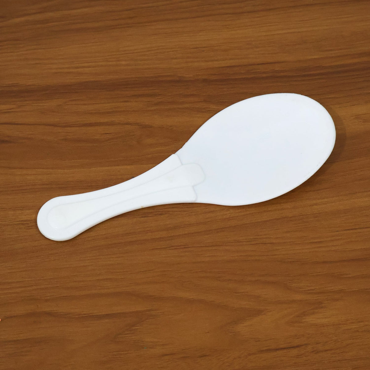 A white plastic rice paddle with a textured handle lies flat on a light brown wooden surface.