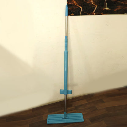A blue and silver flat mop with a grey microfiber pad stands upright against a light wall and dark wooden floor.
