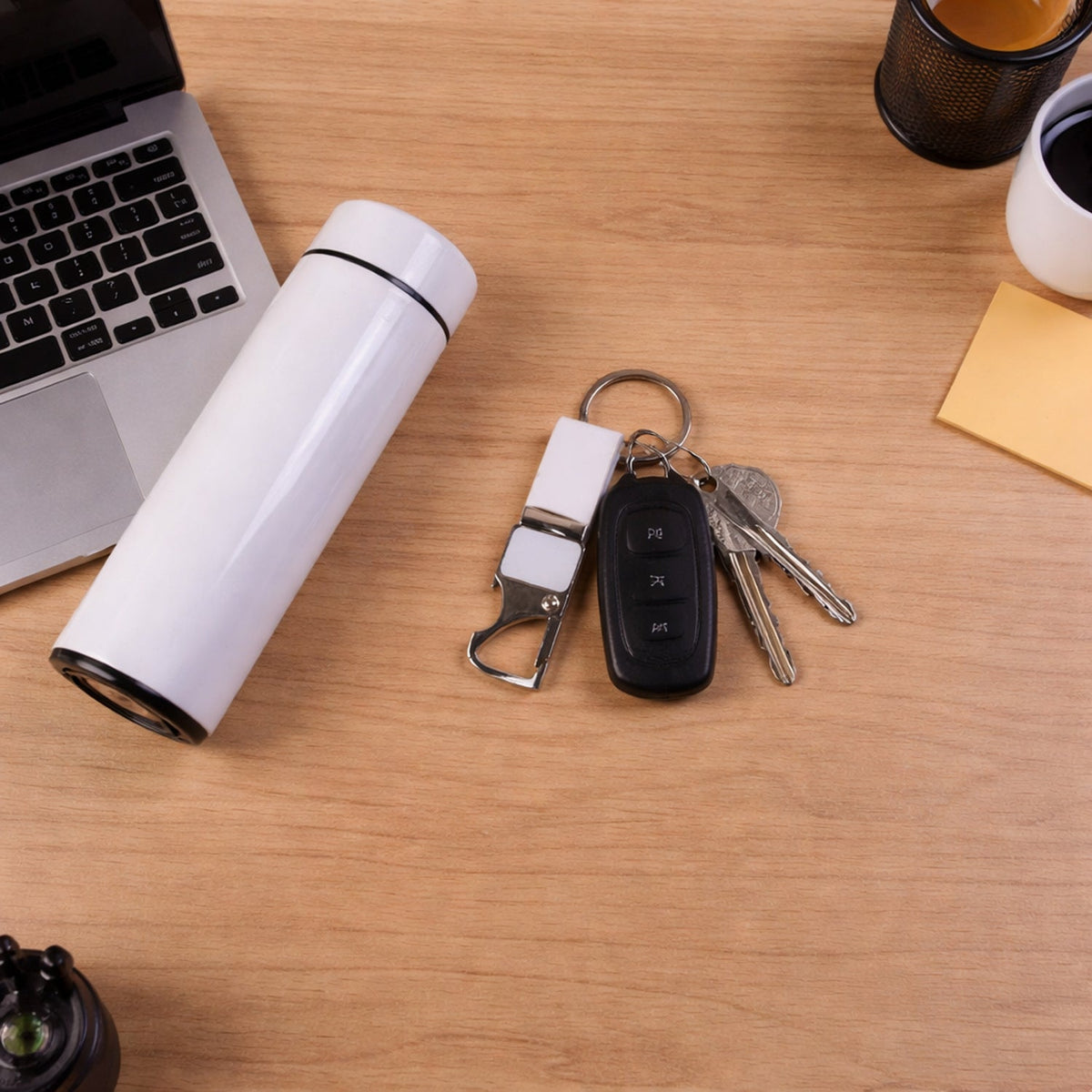 Overhead view of a white thermal bottle, pen, and keychain with car keys on a wooden desk.
