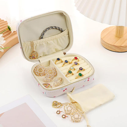 An open cherry print jewelry organizer with rings, earrings, and a necklace, next to a small pouch of jewelry.