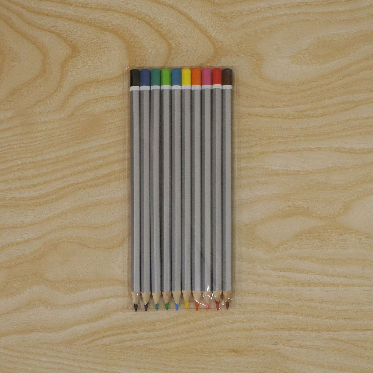 Ten gray hexagonal colored pencils with various tips and ends are sealed in clear plastic packaging on a light wooden