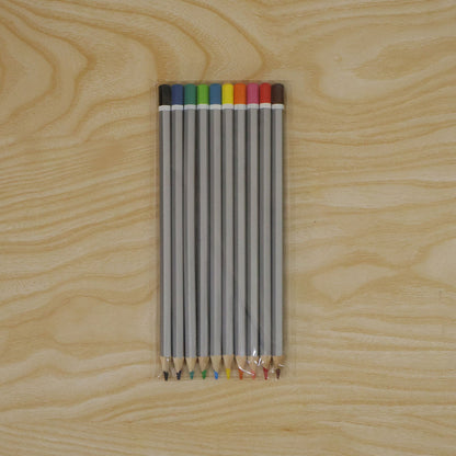 Ten gray hexagonal colored pencils with various tips and ends are sealed in clear plastic packaging on a light wooden