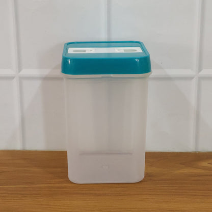 Empty clear plastic food storage container with a teal lid on a wooden surface against a white tiled wall.