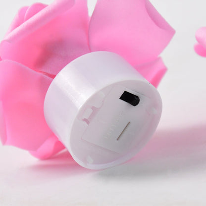 Close-up of the bottom of a white tea light base with a black on/off switch, surrounded by pink rose petals.
