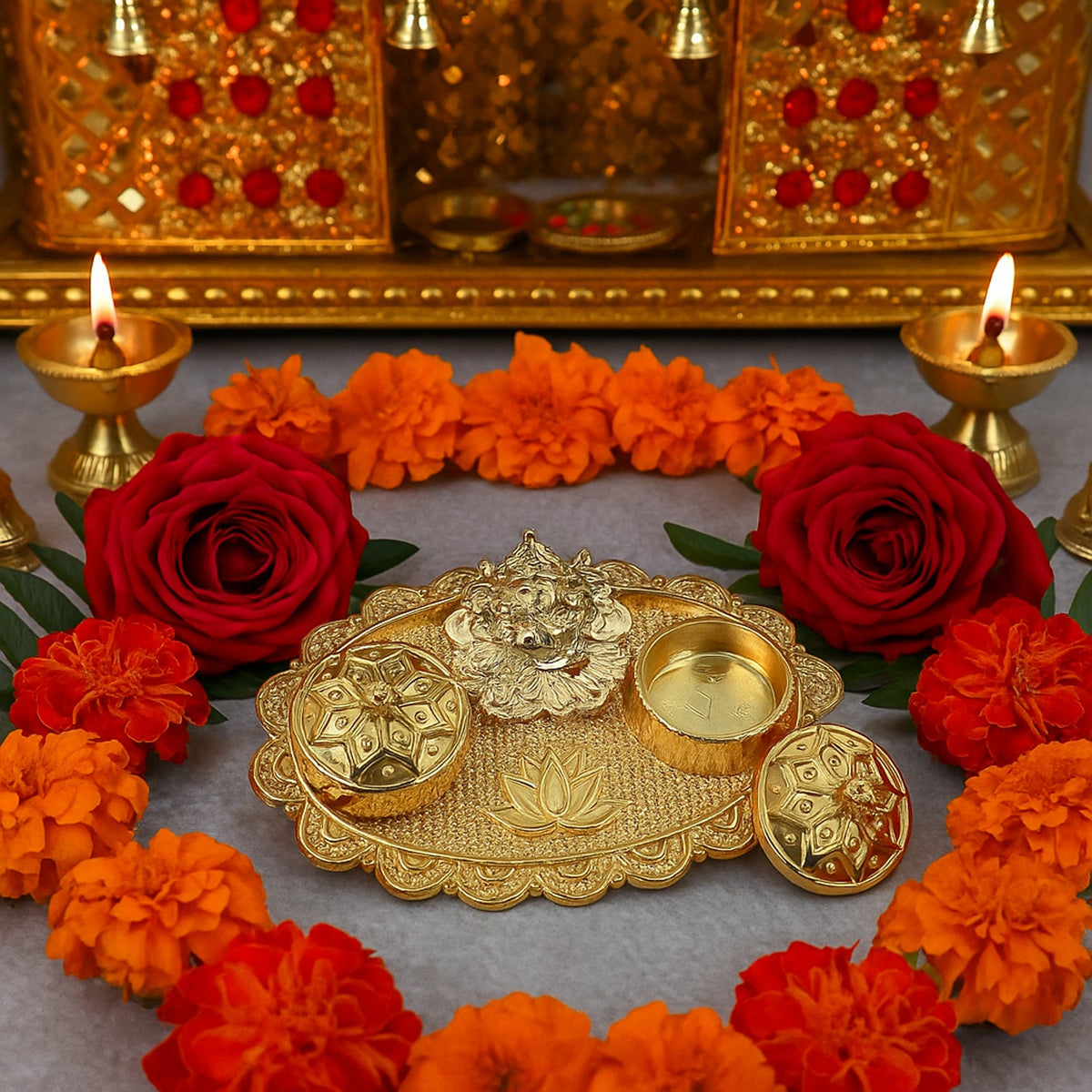 A gold-finished chopra with Ganesh, two containers, and a lotus design, surrounded by red roses, orange marigolds, and lit