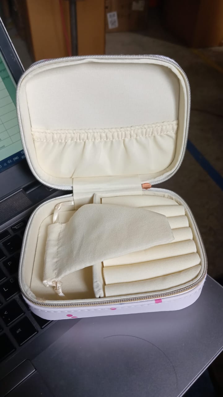 An open cherry print jewelry organizer case with empty compartments and a small pouch, sitting on a laptop.