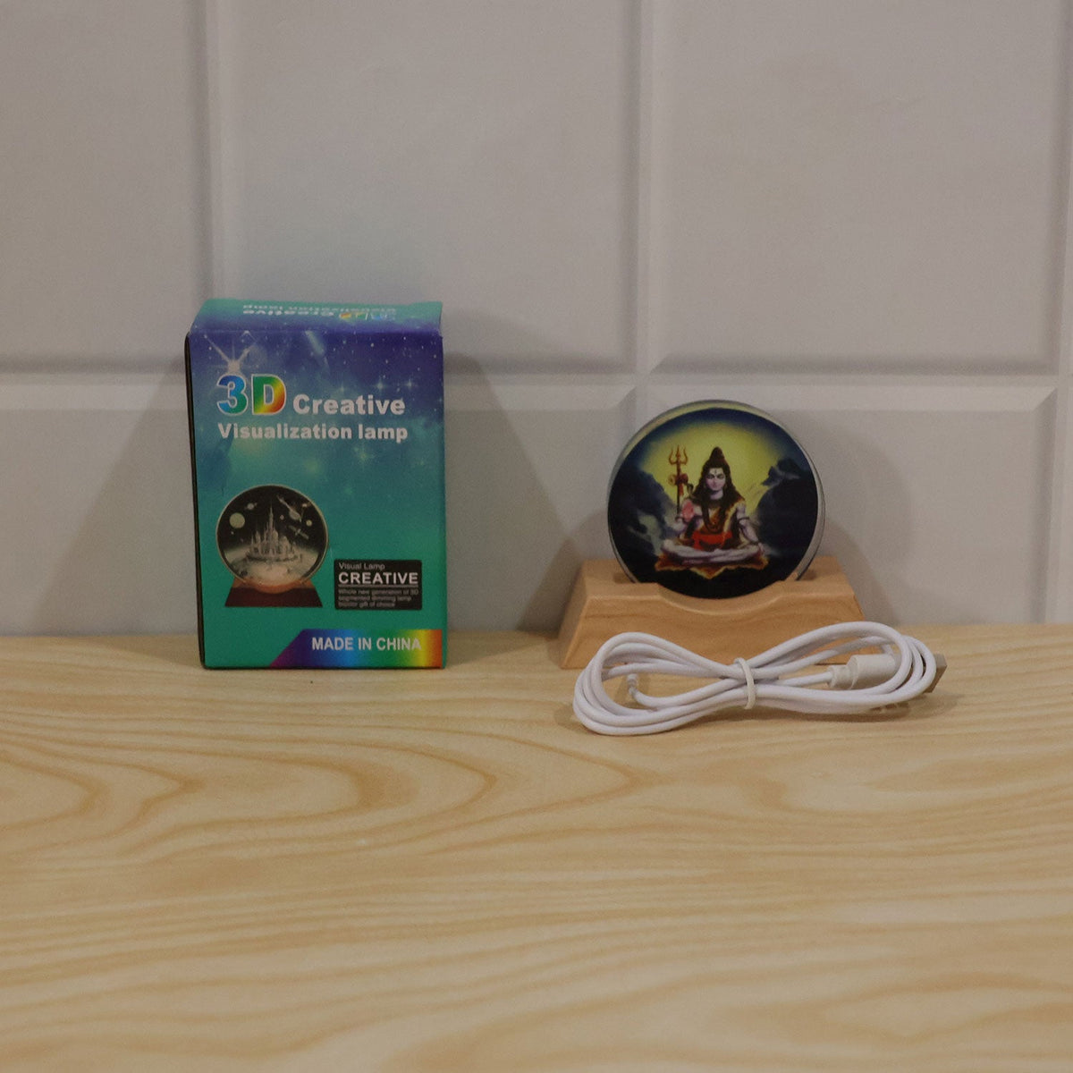 Shiva LED lamp, USB cable, and its blue and green packaging box displayed on a light wooden surface.