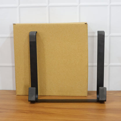 A black metal laptop stand is positioned in front of a brown cardboard box on a wooden surface.
