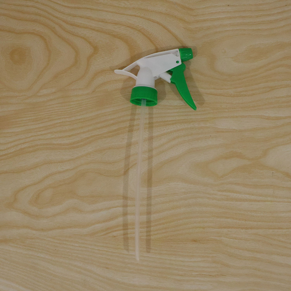 A white and green trigger sprayer nozzle with a long, clear dip tube resting on a light wood surface.