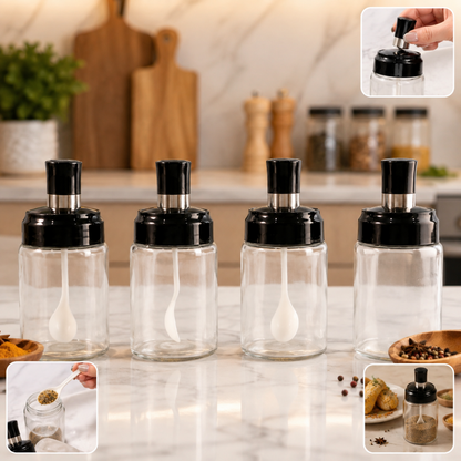 Four transparent spice jars with black lids and white spoons on a kitchen counter with spices.
