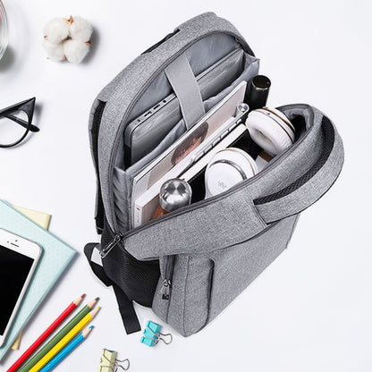 An open grey backpack reveals a laptop, books, headphones, and other accessories on a white desk with office supplies.