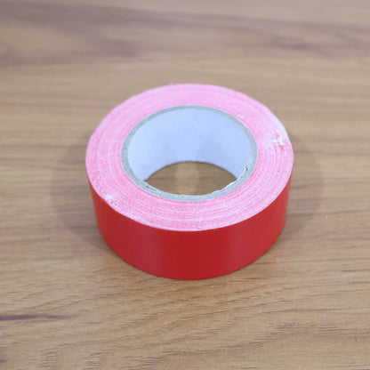 A single roll of red tape on a wooden surface.