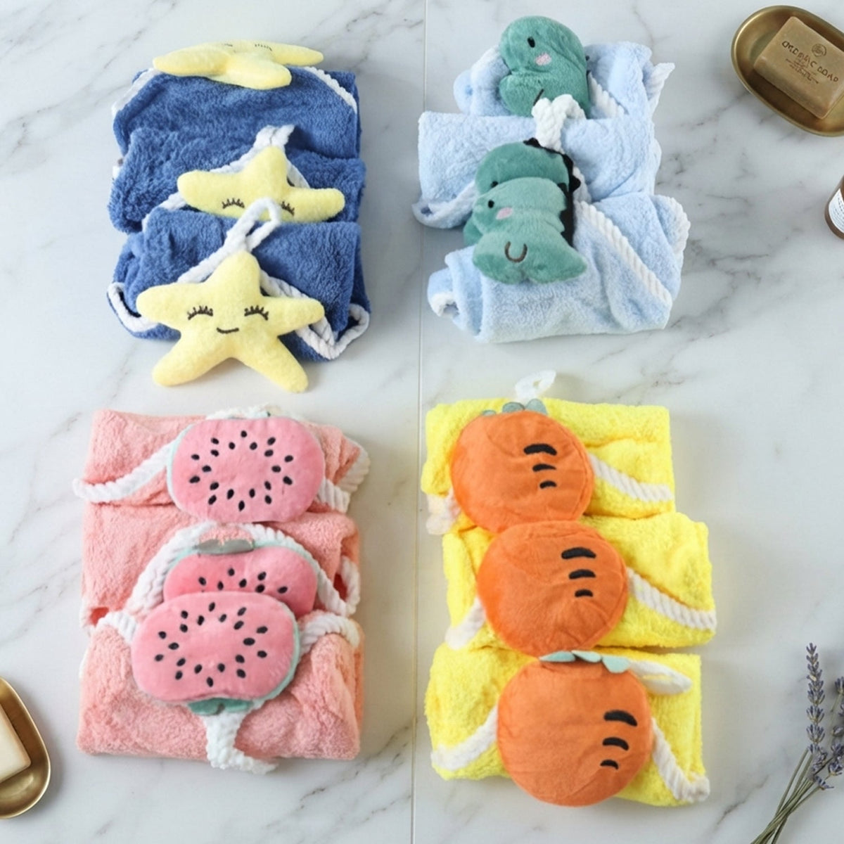 Four stacks of colorful towels with attached plush shapes, arranged on a white marble surface.