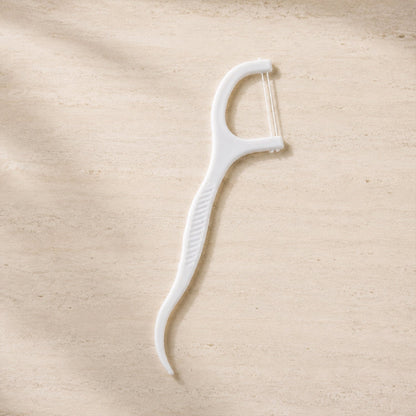 A single white dental floss pick with a textured handle lies on a light brown, textured surface.