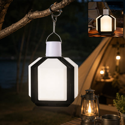 Illuminated white and black foldable LED lantern hanging from a tree branch at night, with a tent in the background.