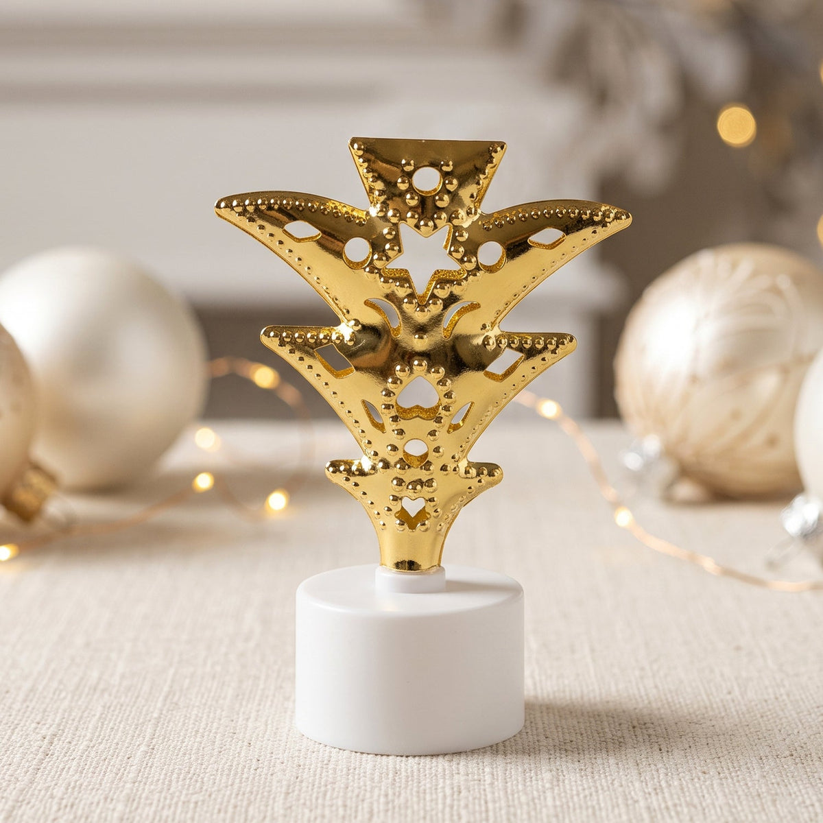 A single golden Christmas tree LED tealight glows brightly against a blurred background of white ornaments.