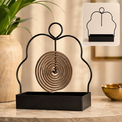 A black metal mosquito coil holder with a brown spiral coil sits on a marble surface next to a plant.