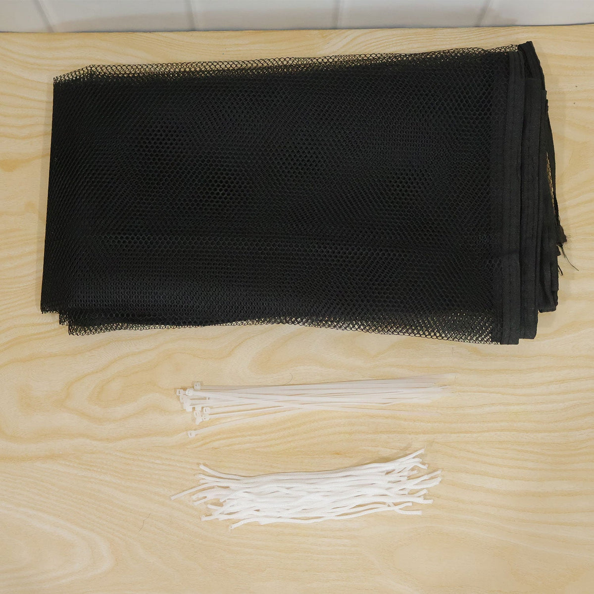 A folded black mesh safety net, white cable ties, and white fastening cords are neatly arranged on a light wooden surface.