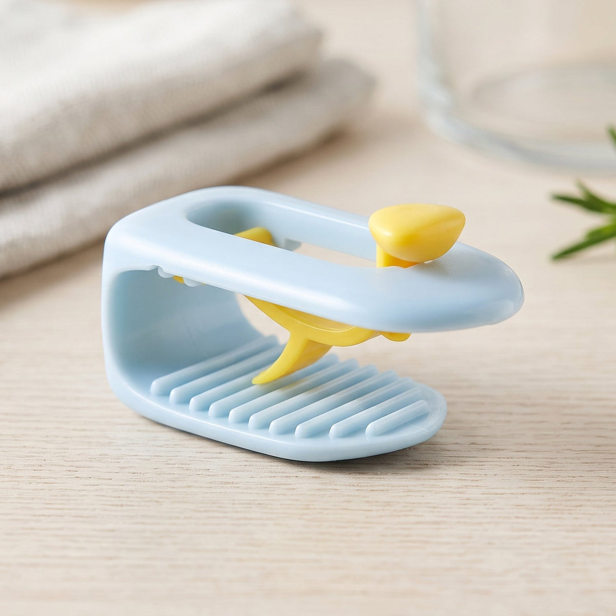 A single blue and yellow plastic clip rests on a light wooden surface, with a blurred background of kitchen items.