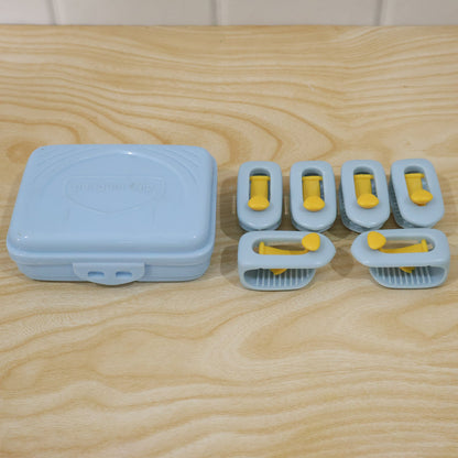 A light blue plastic storage case and six blue and yellow plastic clips are arranged on a light wooden surface.