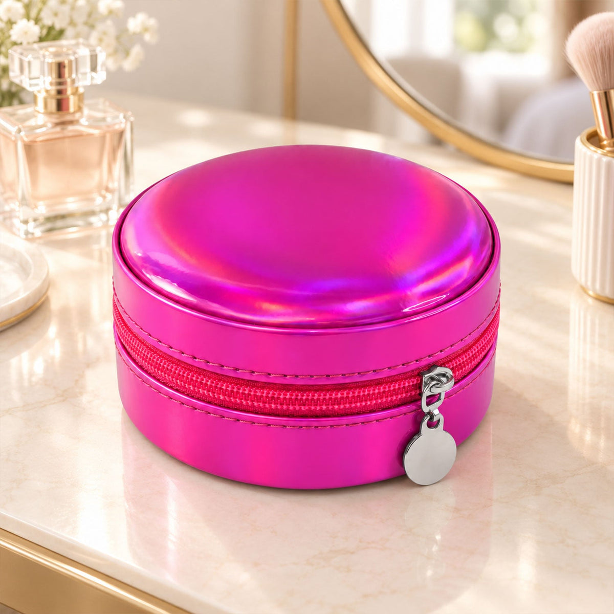 Closed round holographic pink jewellery box with a silver zipper pull, resting on a white marble surface.