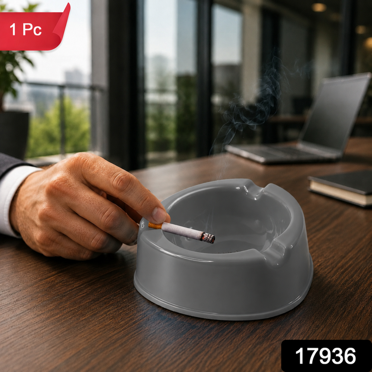 A person's hand holding a lit cigarette over a grey plastic ashtray on a wooden desk, with a red "1 Pc" label in the corner.