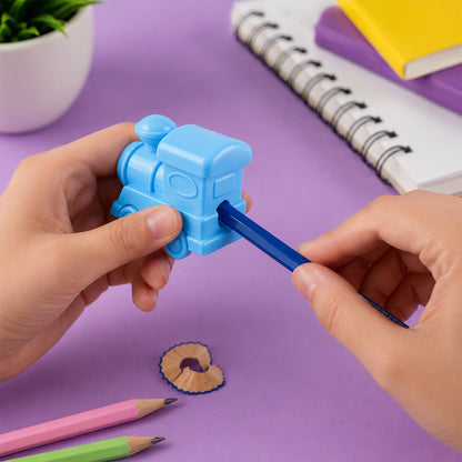 Hands sharpening a dark blue pencil with a light blue train-shaped sharpener on a purple surface with pencil shavings.