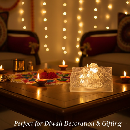 A clear LED iceberg light glows on a wooden table surrounded by small lit diyas and a colorful rangoli mat.