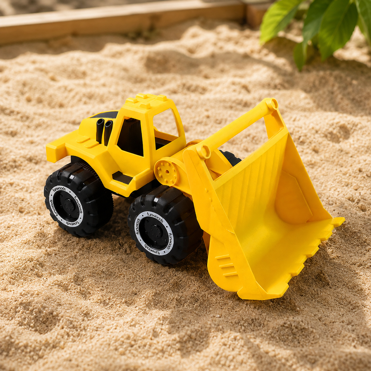A bright yellow plastic toy front-end loader with black wheels sits in a sandy sandbox.