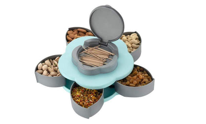 A hand opens the light blue petal-shaped container, revealing five compartments filled with marshmallows, candies, and