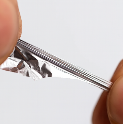 Two fingers stretching a thin, shiny piece of aluminum foil, showing its flexibility and texture.