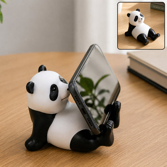 A black and white panda figurine holds a black smartphone vertically on a wooden desk. Inset shows the panda without the