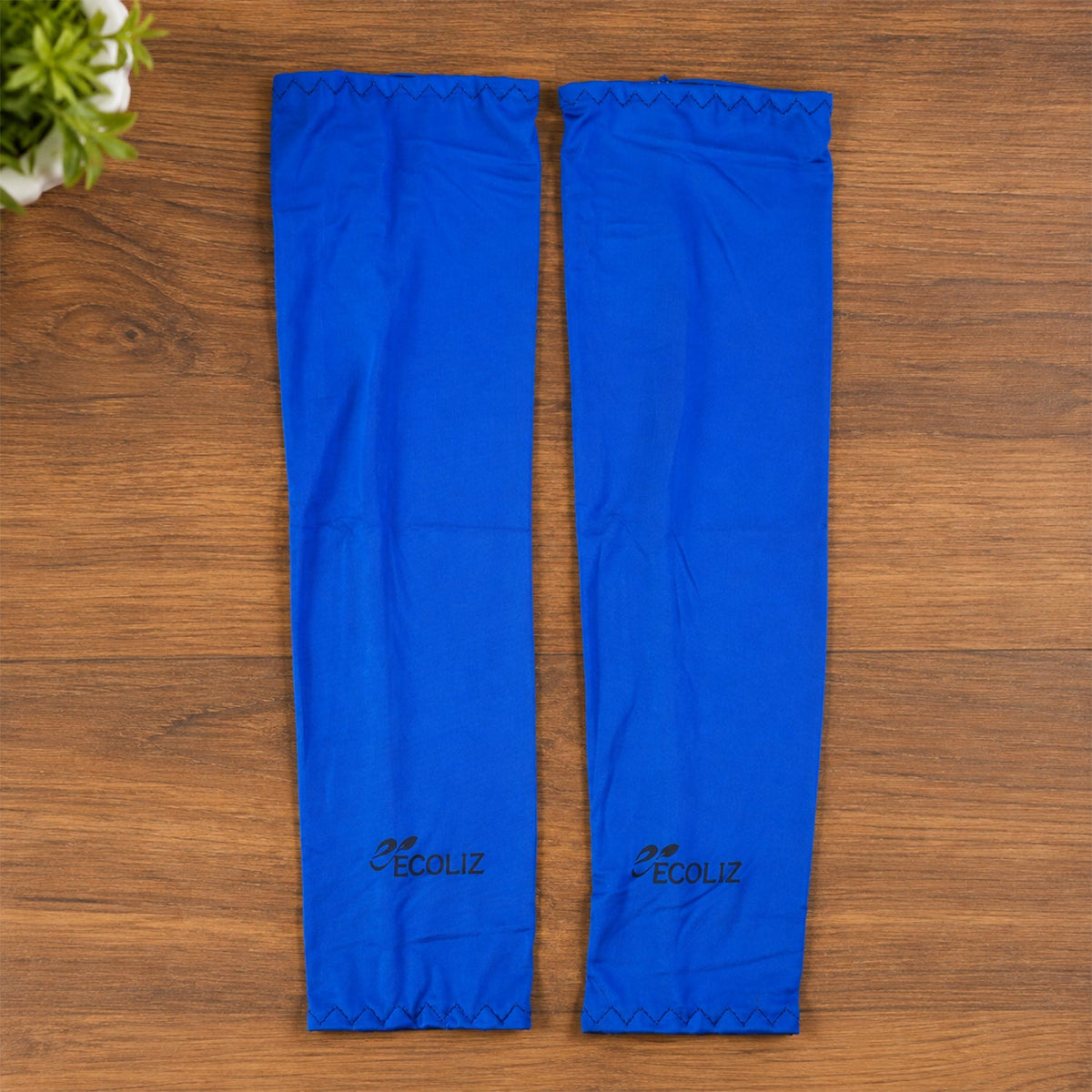 Two blue arm sleeves with the Ecoliz logo laid flat on a wooden surface next to a green plant.