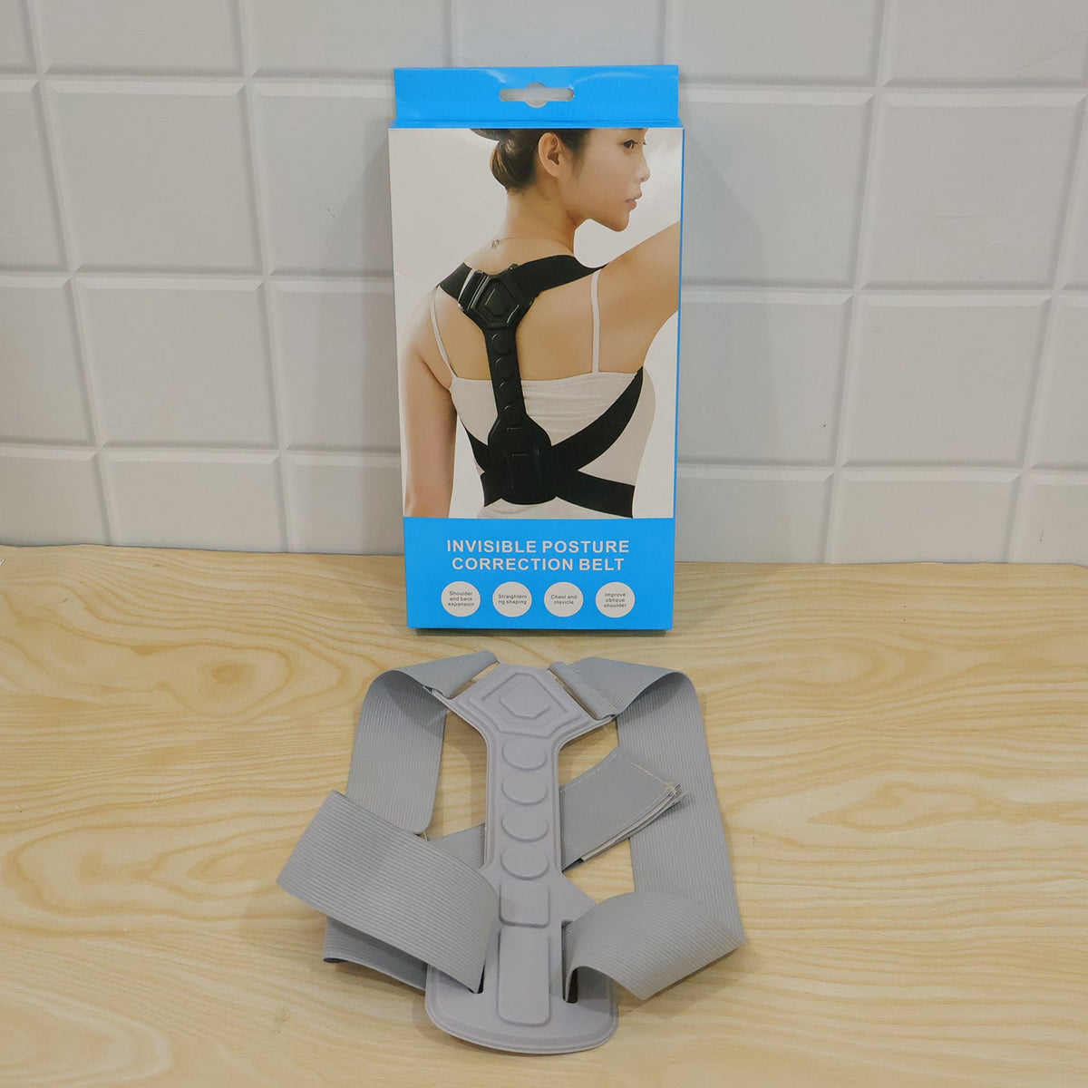 A grey posture corrector belt laid out in front of its blue and white retail box on a wooden surface.
