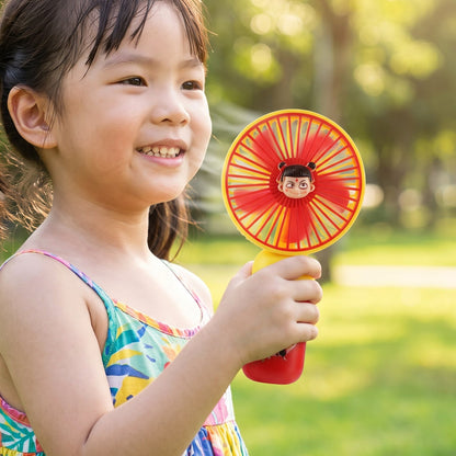A young girl smiling and holding a red and yellow mini fan with a cartoon character face in the center. – view 3