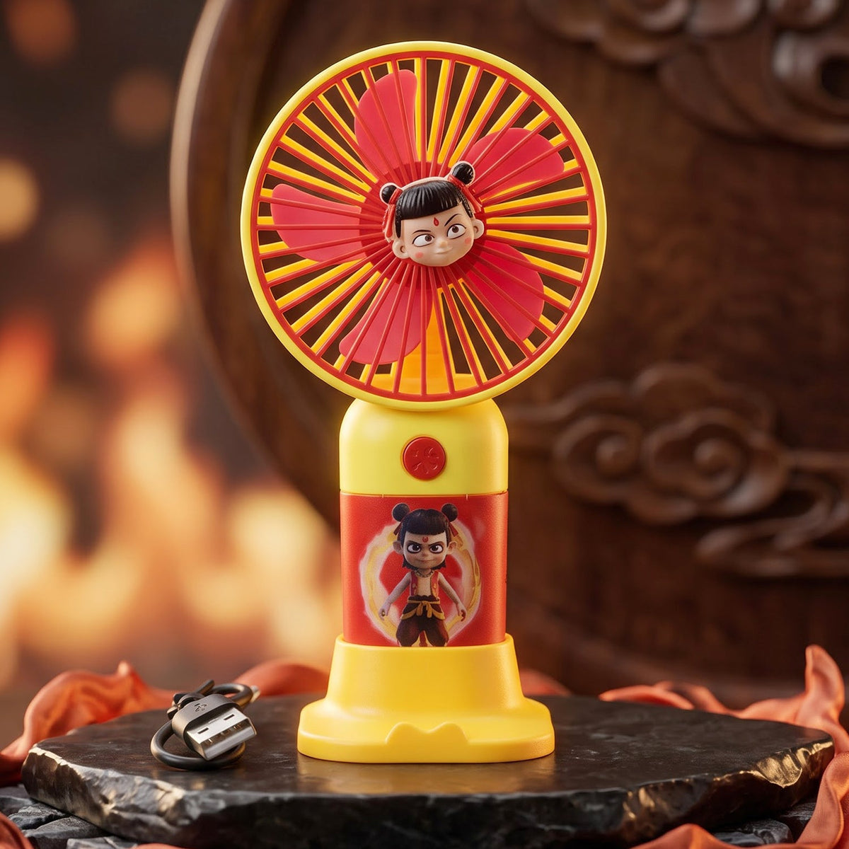 A red and yellow mini fan with a cartoon character and stand, with a USB cable on a dark textured surface.