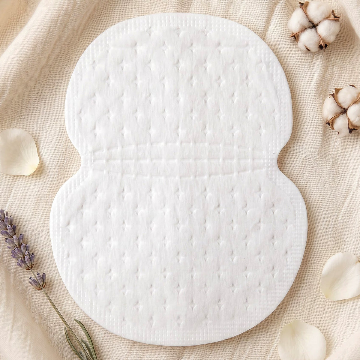A single white, textured sweat pad on a light fabric background, surrounded by cotton bolls and lavender sprigs.