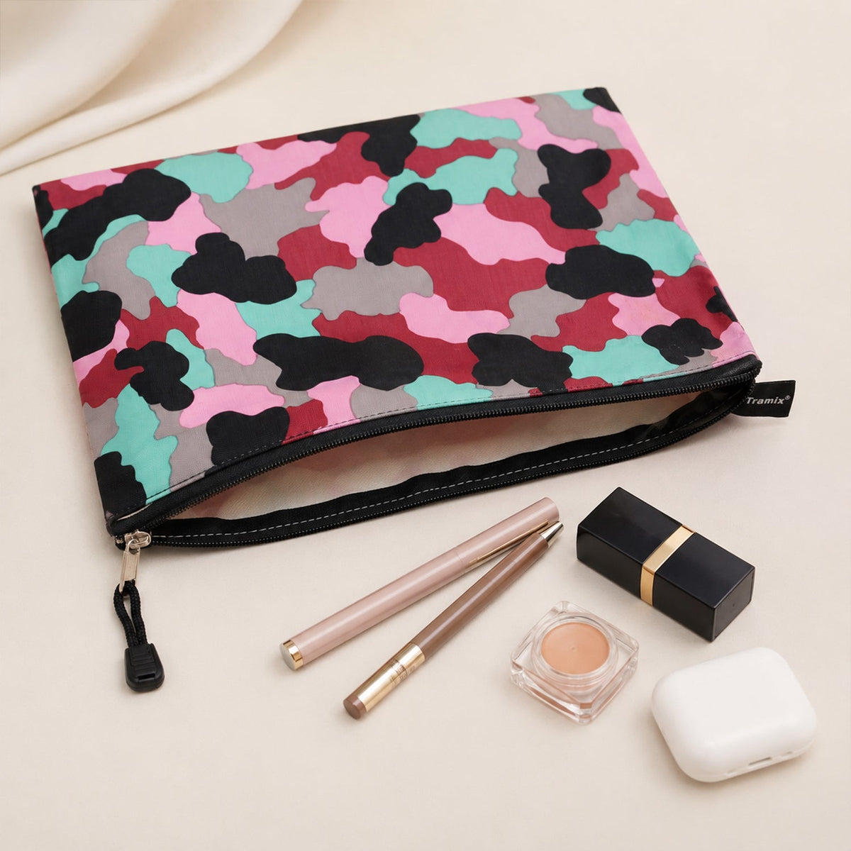 An open pouch with a pink, red, black, grey, and teal camouflage pattern, revealing its interior and surrounded by makeup