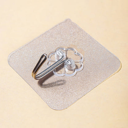 A close-up, angled view of a transparent self-adhesive hook with a silver metal hook on a light brown surface.