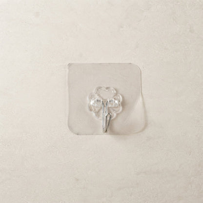 A transparent self-adhesive hook with a silver metal hook centered on a light beige tiled wall.