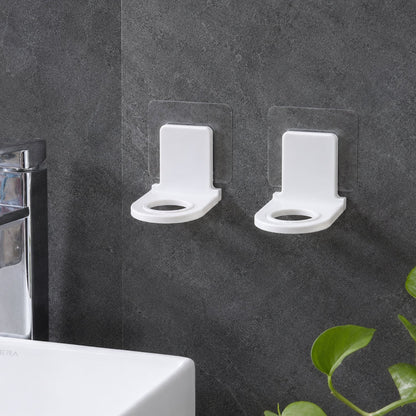 Two white plastic bottle holders with clear adhesive pads lying on a light gray tiled floor beside a white bathtub.