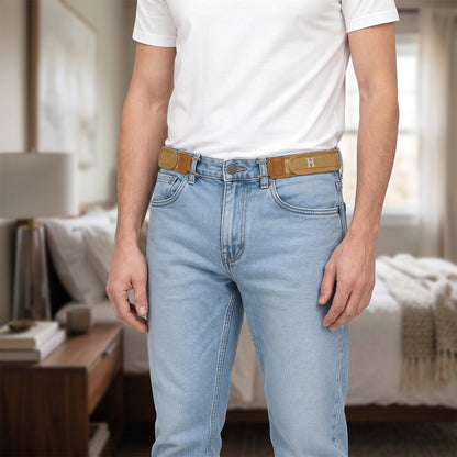 A man wearing light wash jeans and a white t-shirt, with two tan elastic belt hooks attached to his jeans, in a bedroom