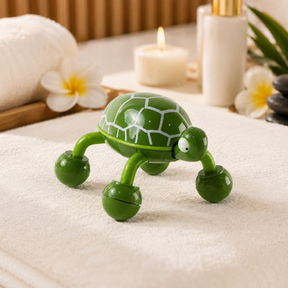 A green turtle-shaped massager with white shell patterns sits on a white towel next to a lit candle and spa items.